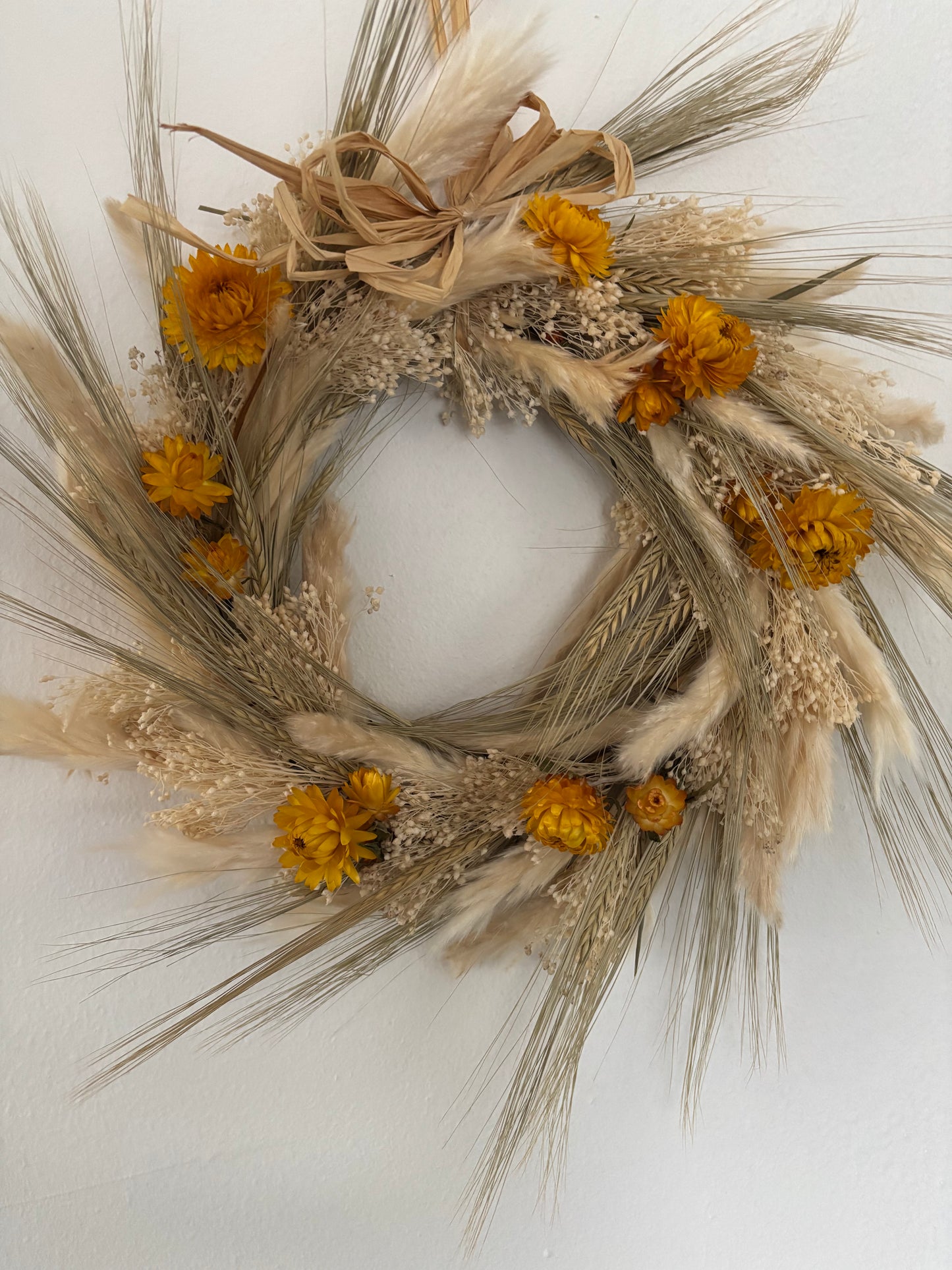 Front facing view of ivory, yellow dried flower and grasses wreath