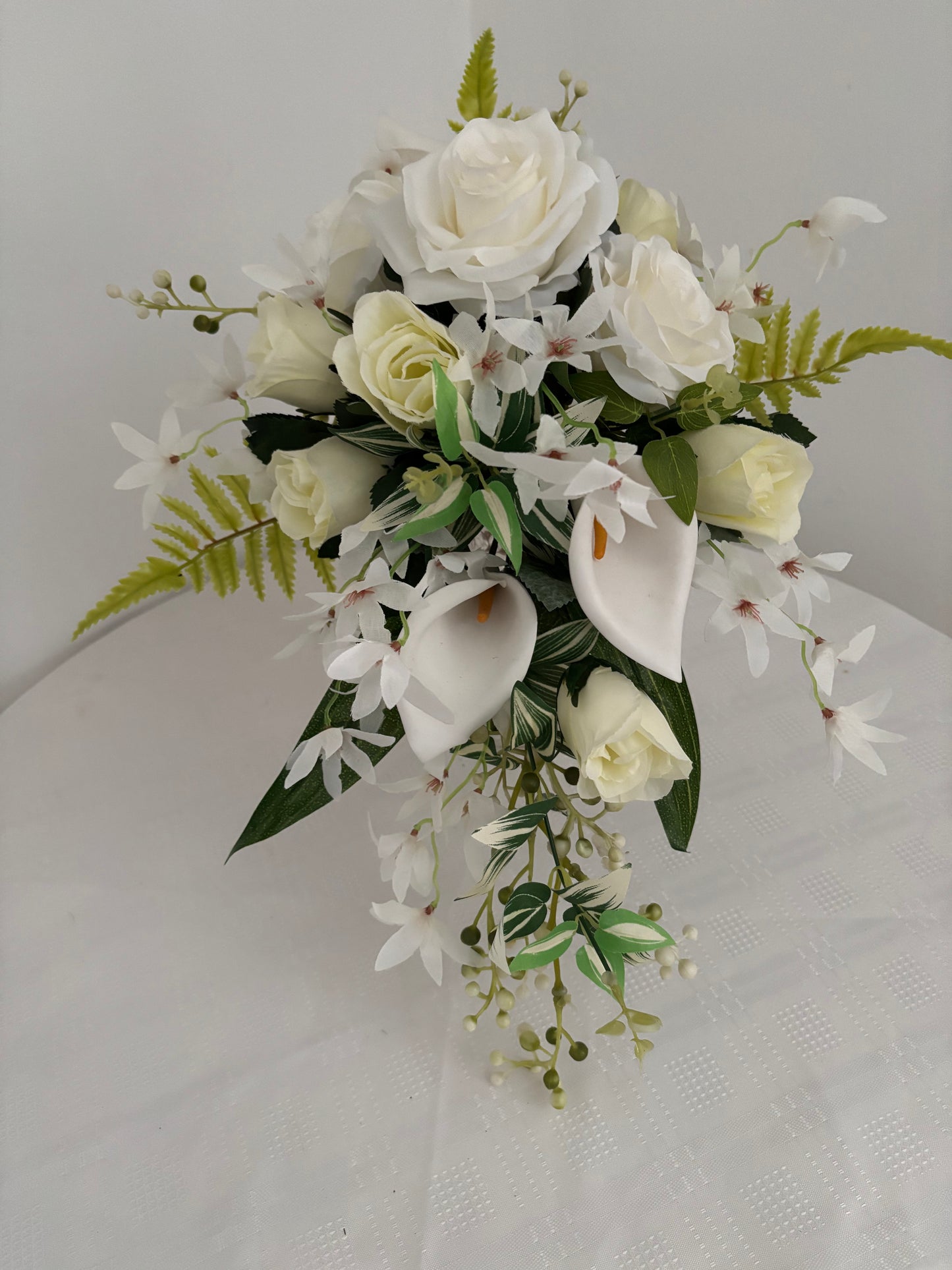 Silk artificial bridal shower bouquet of pale ivory rose buds, white open garden roses and lilies surrounded by blossoms, mixed greenery with eucalyptus.