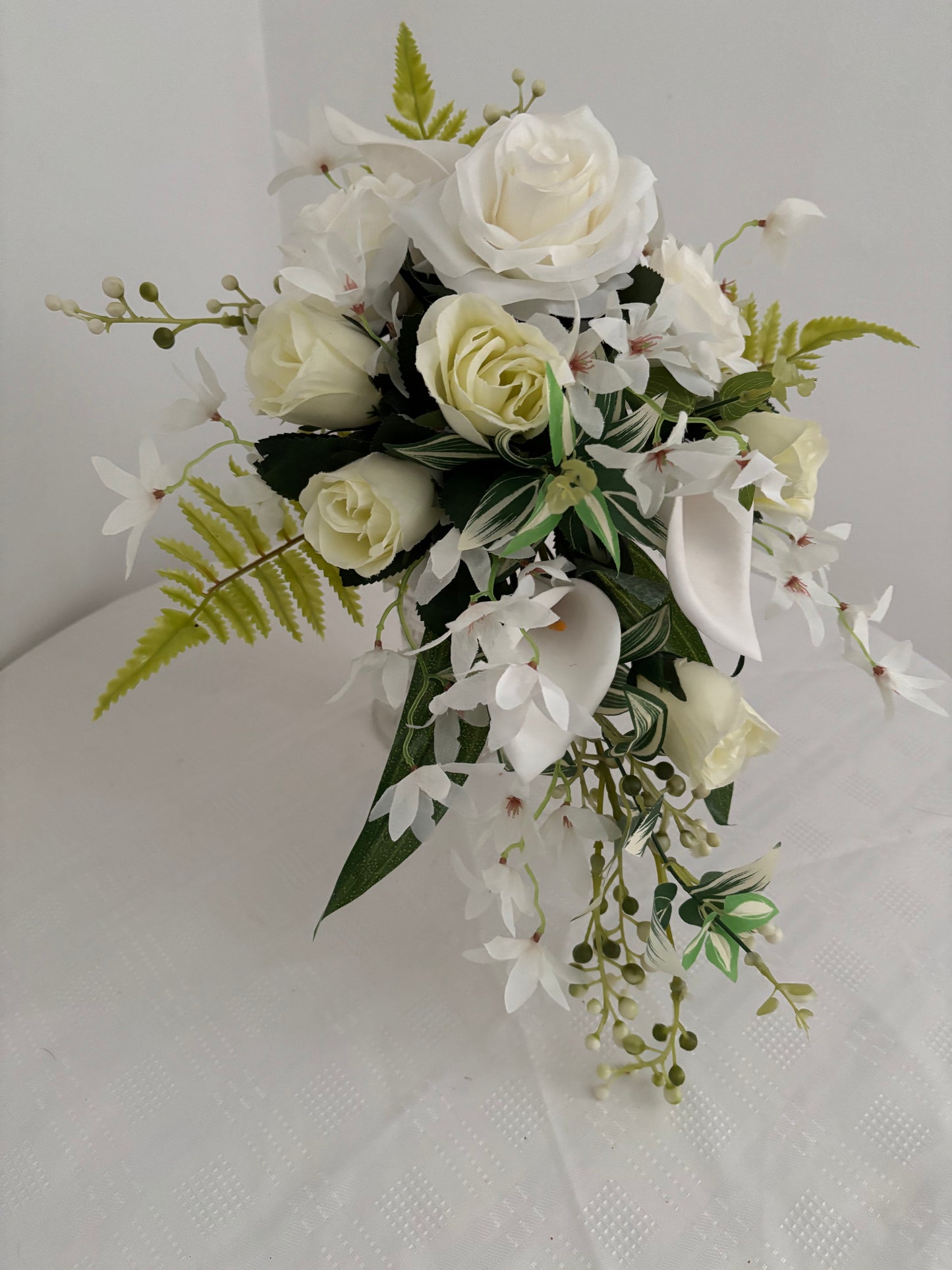 Silk artificial bridal shower bouquet of pale ivory rose buds, white open garden roses and lilies surrounded by blossoms, mixed greenery with eucalyptus.