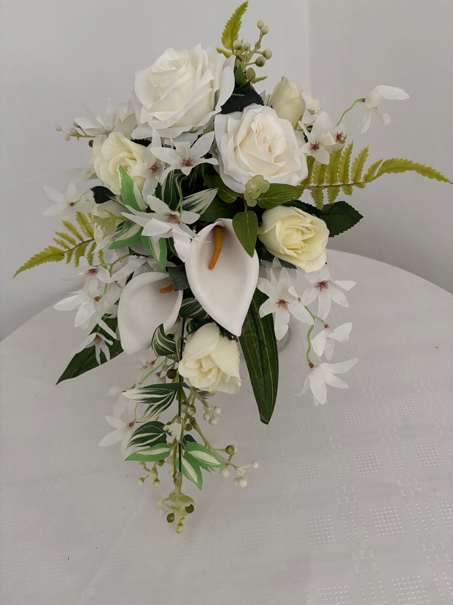 Silk artificial bridal shower bouquet of pale ivory rose buds, white open garden roses and lilies surrounded by blossoms, mixed greenery with eucalyptus.