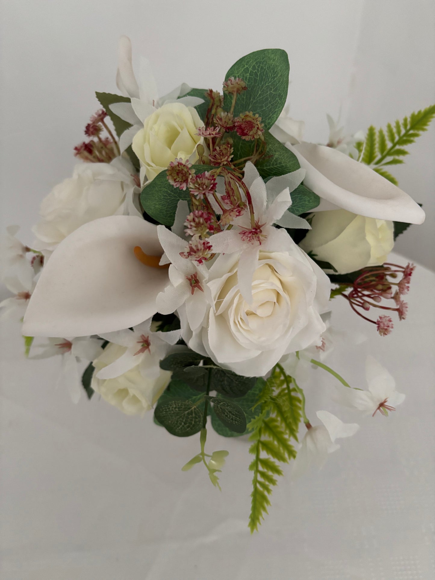 Silk artificial bride or bridesmaids post bouquet of pale ivory rose buds white open garden roses and lilies surrounded by mixed greenery with eucalyptus.