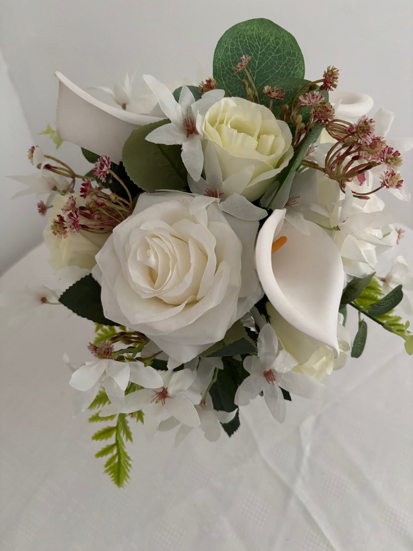 Silk artificial bride or bridesmaids post bouquet of pale ivory rose buds white open garden roses and lilies surrounded by mixed greenery with eucalyptus.