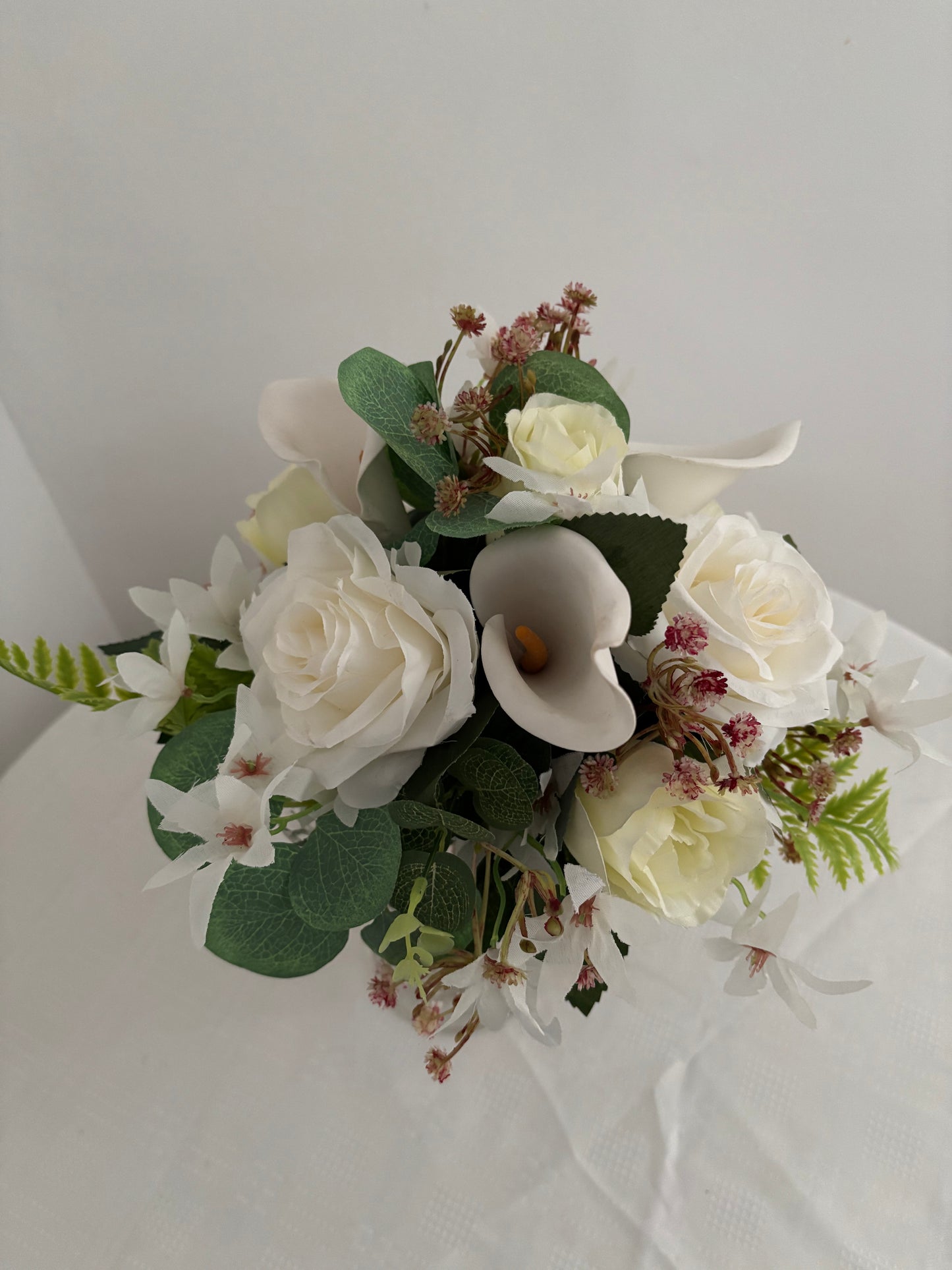 Silk artificial bride or bridesmaids post bouquet of pale ivory rose buds white open garden roses and lilies surrounded by mixed greenery with eucalyptus.