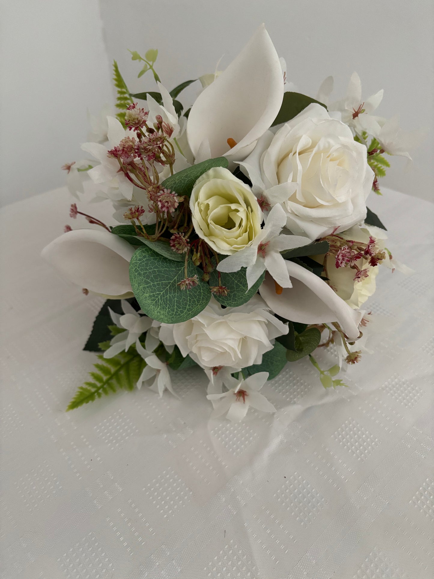 Silk artificial bride or bridesmaids post bouquet of pale ivory rose buds white open garden roses and lilies surrounded by mixed greenery with eucalyptus.