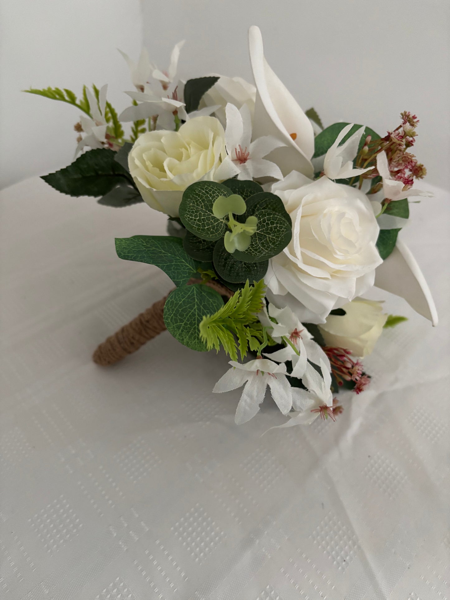 Silk artificial bride or bridesmaids post bouquet of pale ivory rose buds white open garden roses and lilies surrounded by mixed greenery with eucalyptus.