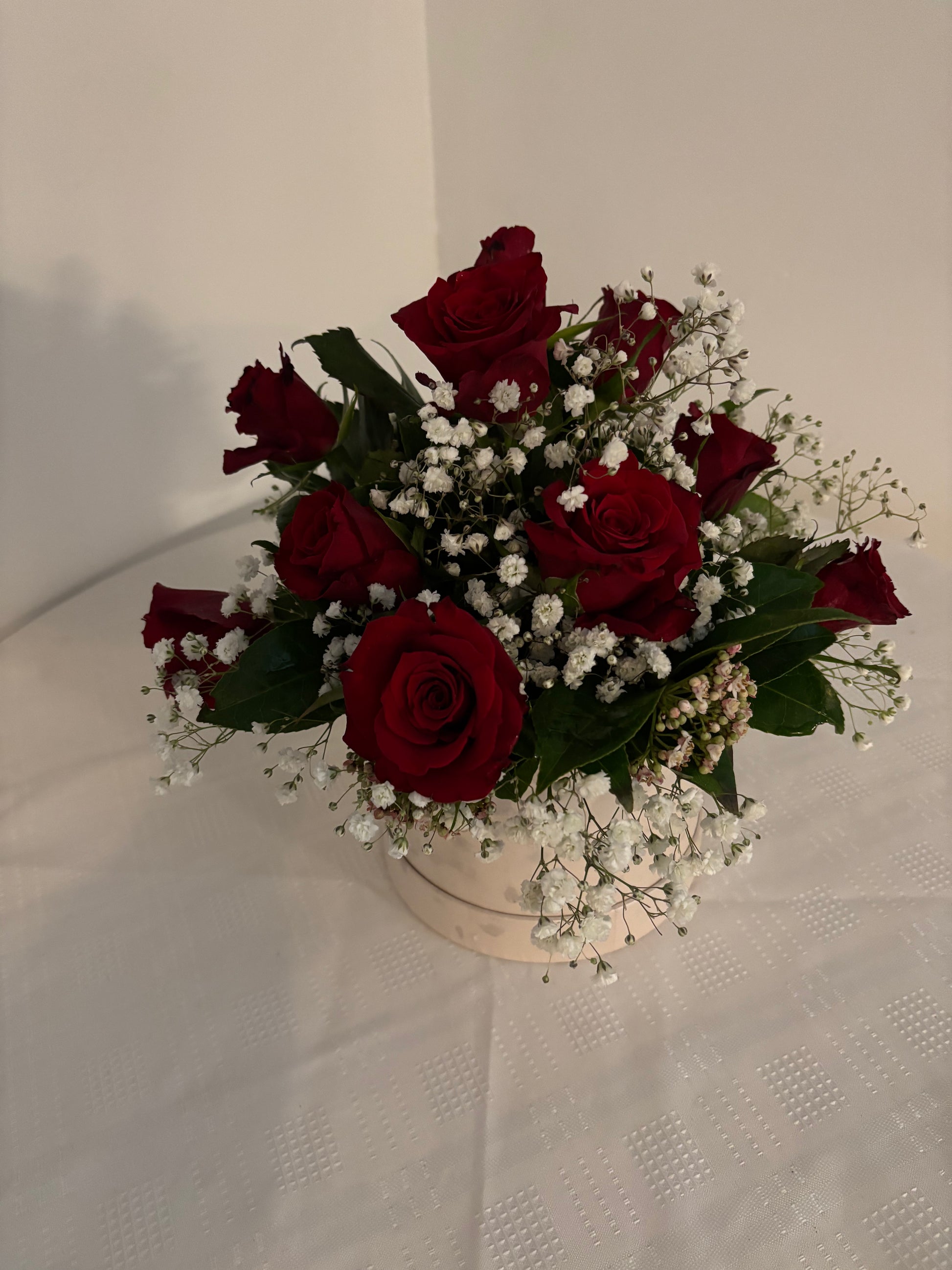 Arrangement of red roses and white gypsophila in a cream coloured hat box