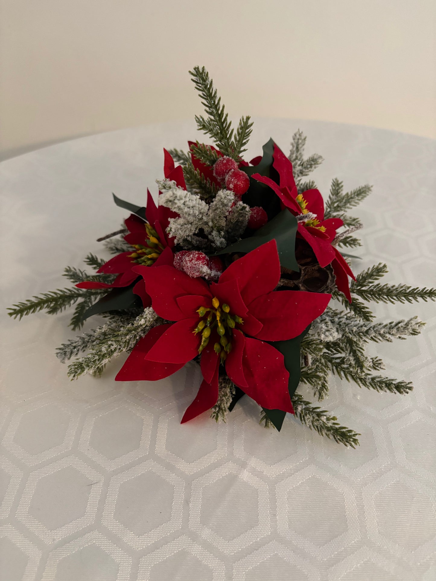 A festive Christmas centerpiece featuring 3 bright red silk poinsettias, artificial frosted green spruce branches, and  foliage.