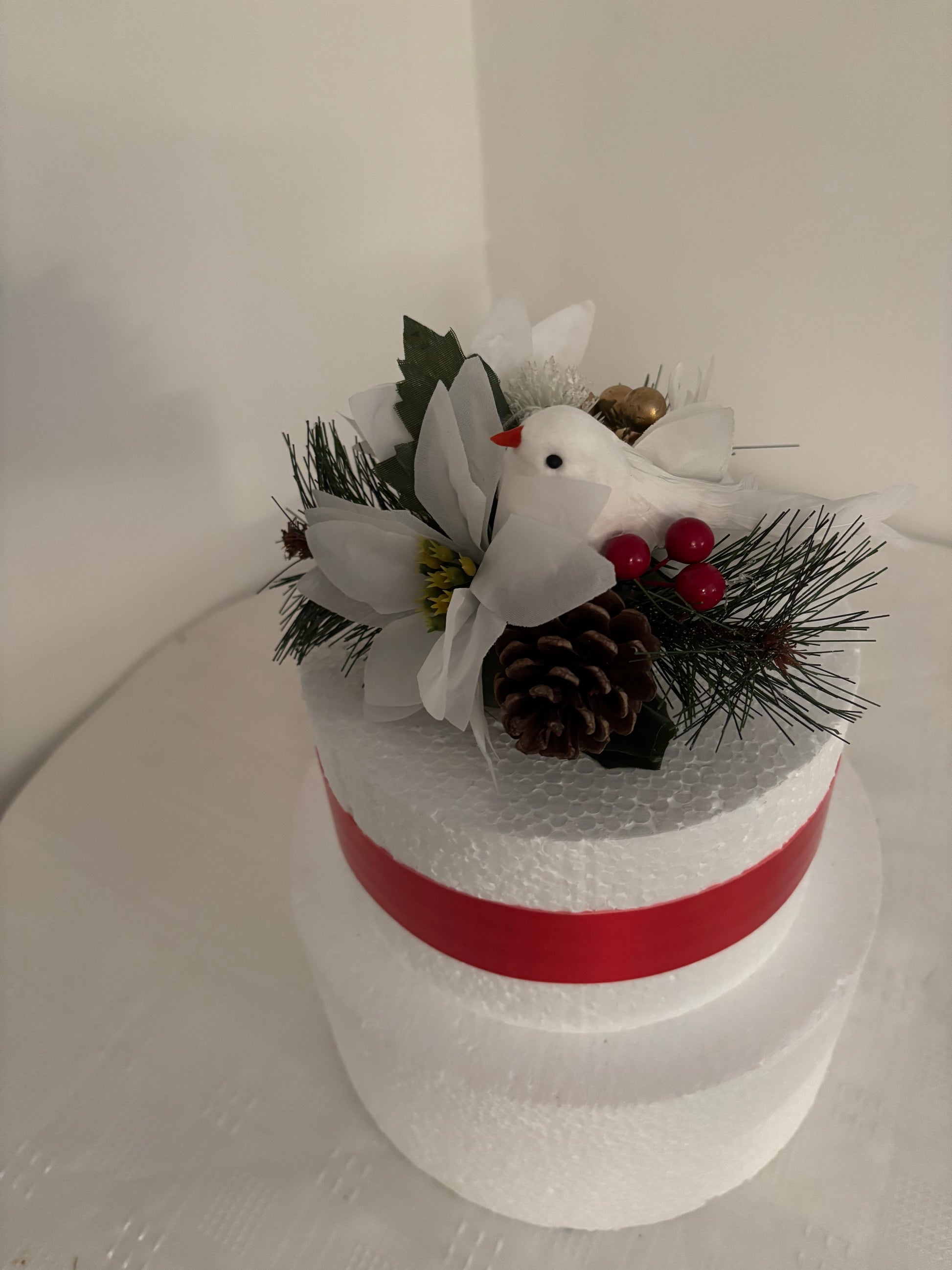 Decorative festive cake topper with a white dove, pine cones, and white poinsettia.