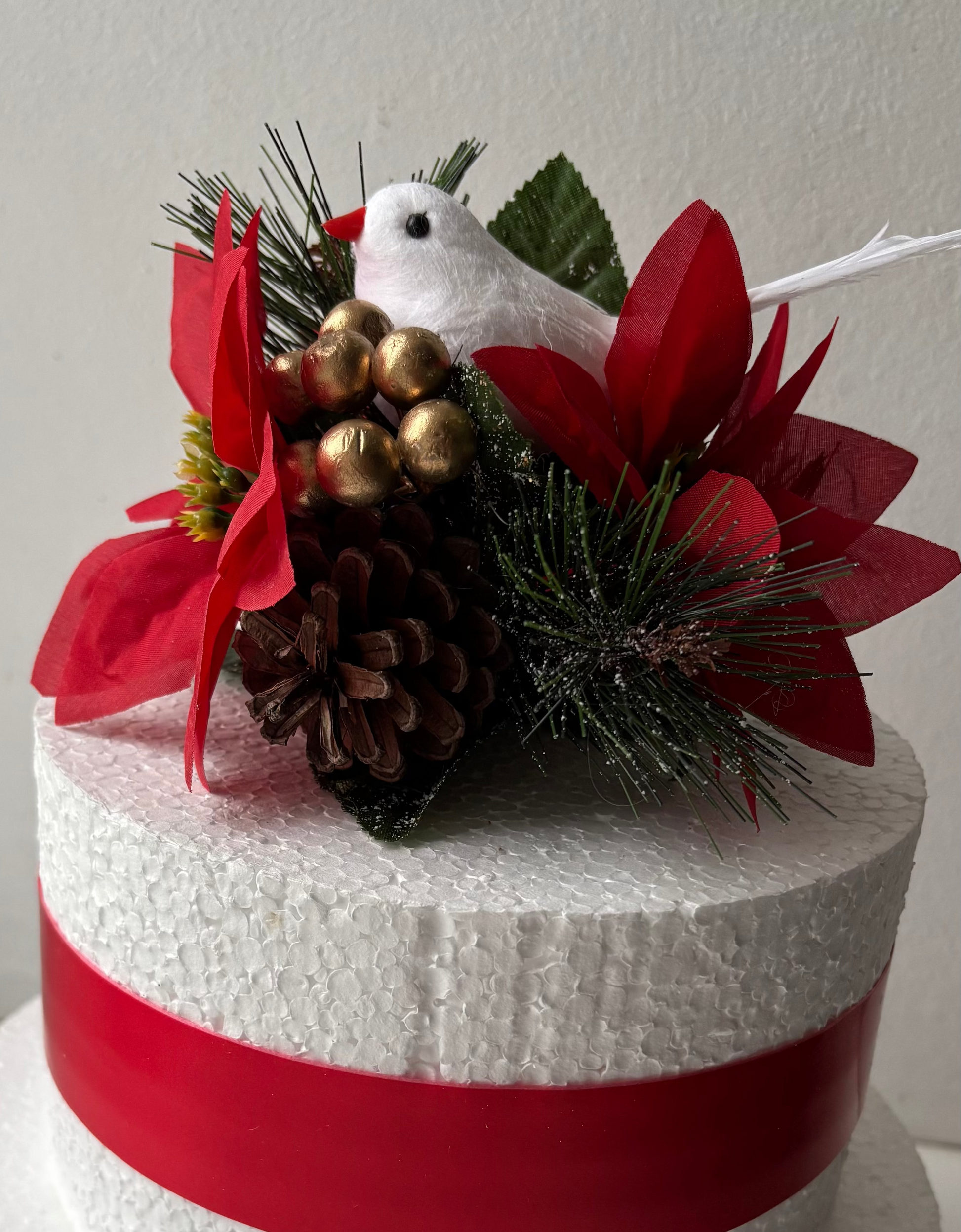 Decorative cake topper with a white dove, red flowers, and pinecones on a plain background